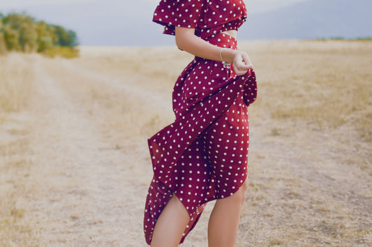 woman in red dress standing on rock formation near body of water during daytime